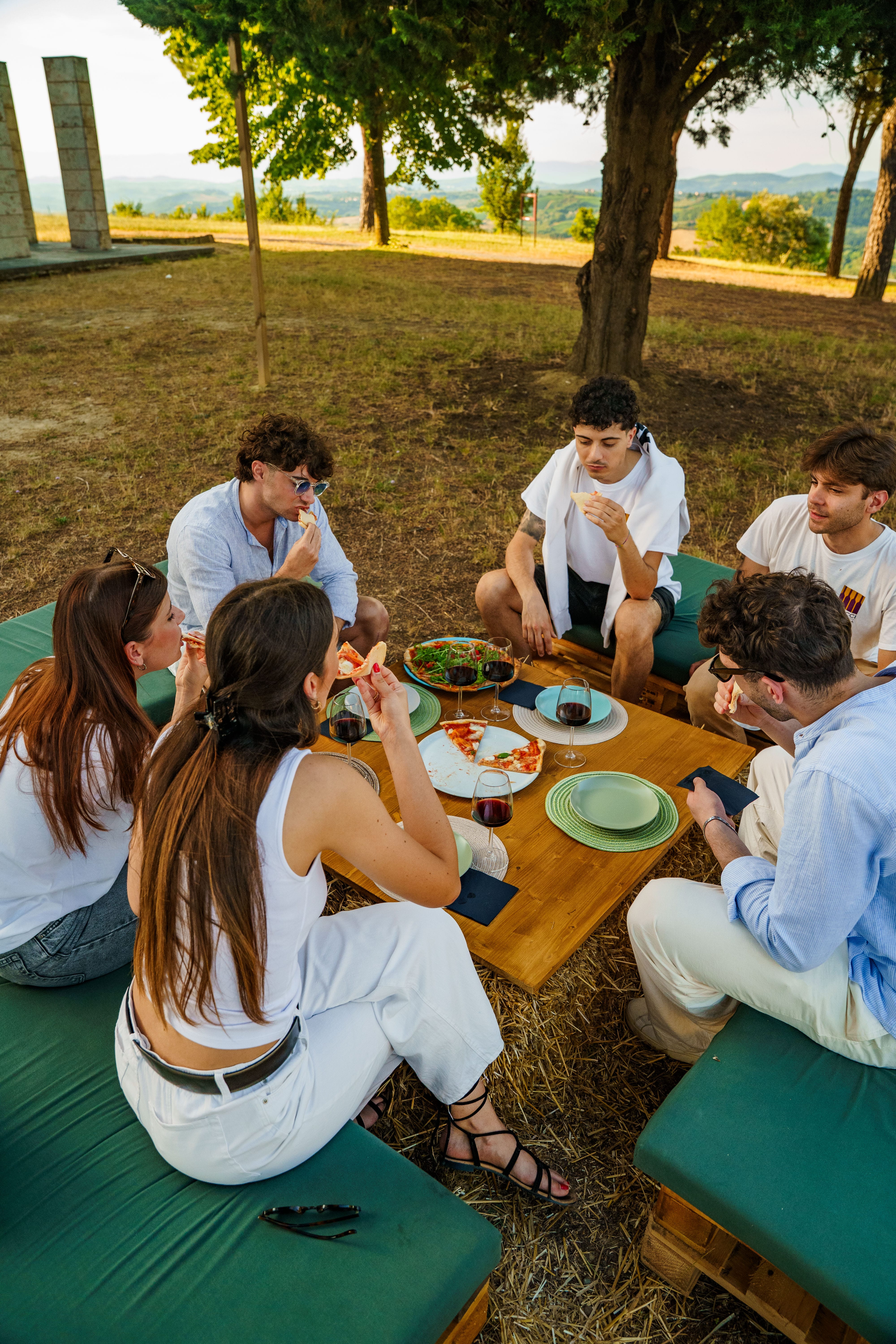 Gruppo di amici a cena all'aperto tra i lecci